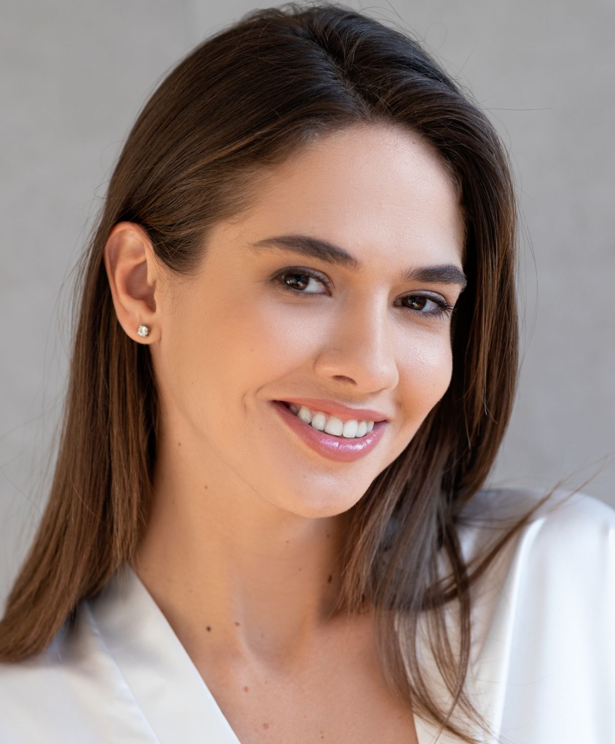 Smiling woman in white top against gray background.