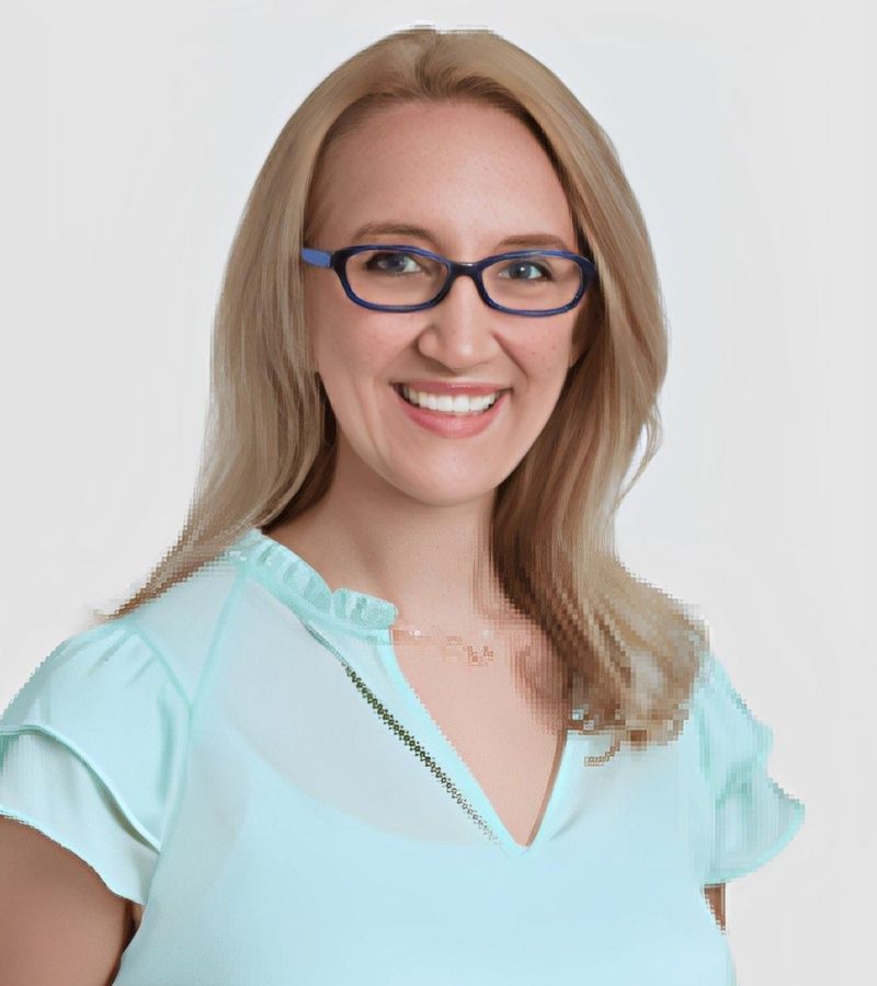 Smiling woman with glasses in light blue shirt.